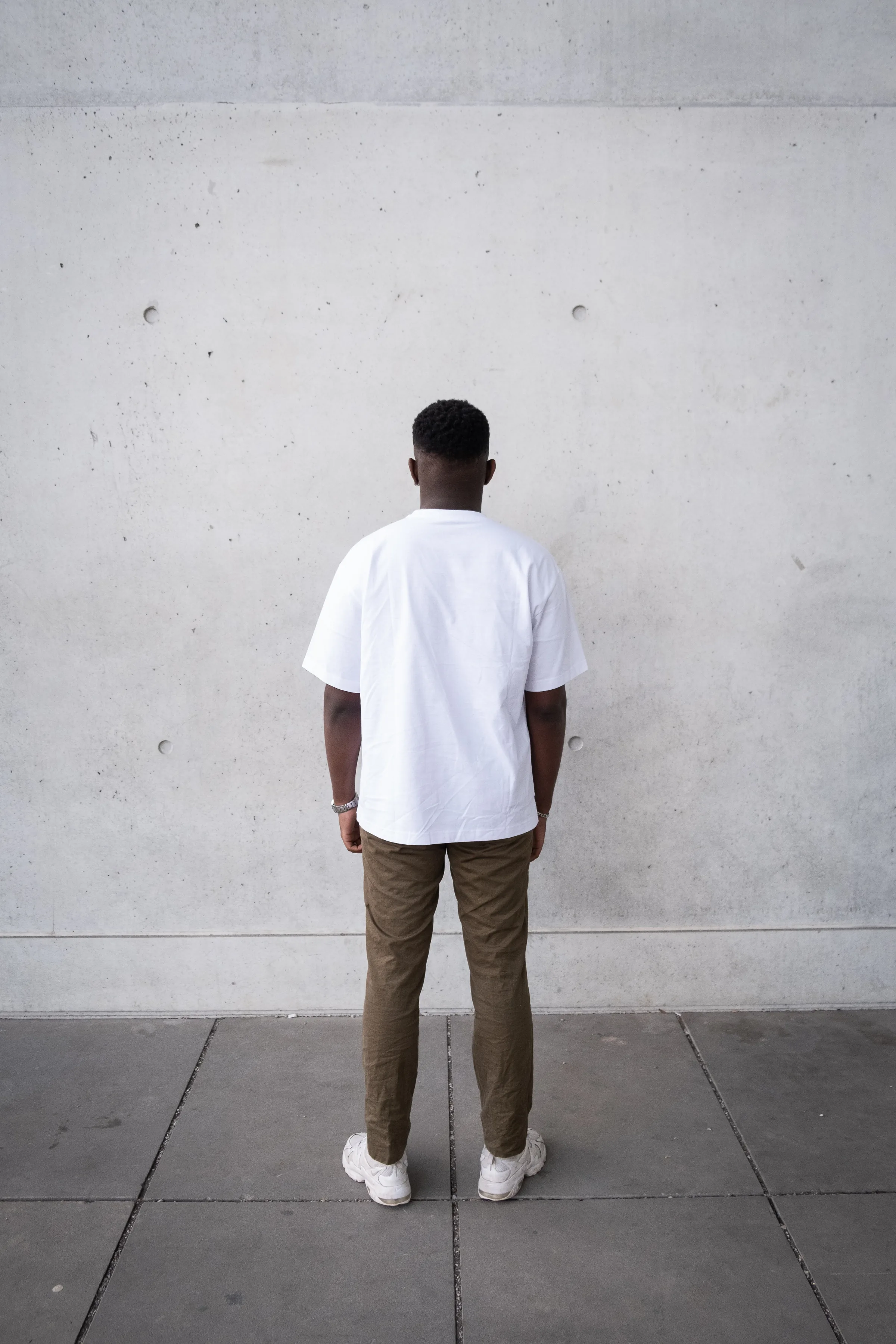 Person in weißem T-Shirt steht frontal vor einer Betonwand