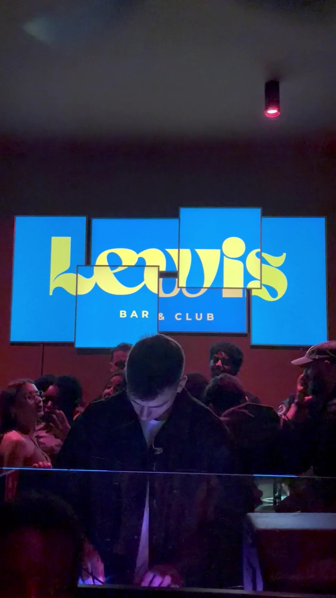 Gäste vor beleuchteten Screens mit dem Schriftzug „Lewis Bar & Club“ auf einem White-Lotus-Event